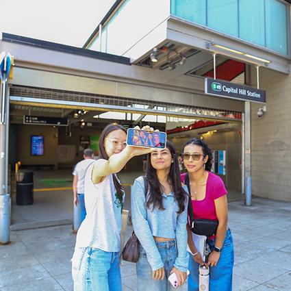 Three individuals take a selfie in front of the entrance to the Capital Hill Station.