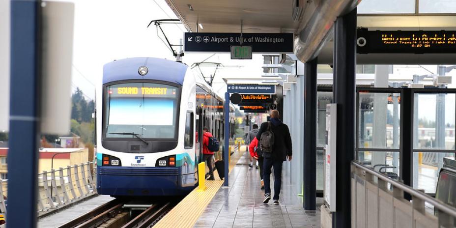 At the train station, two riders walk towards the oncoming train. 